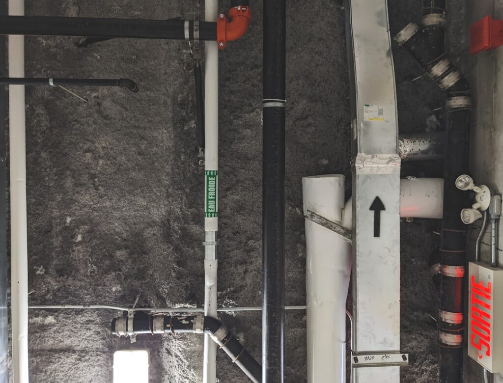 A technician installs a white PVC radon vent pipe in a residential basement utility area.