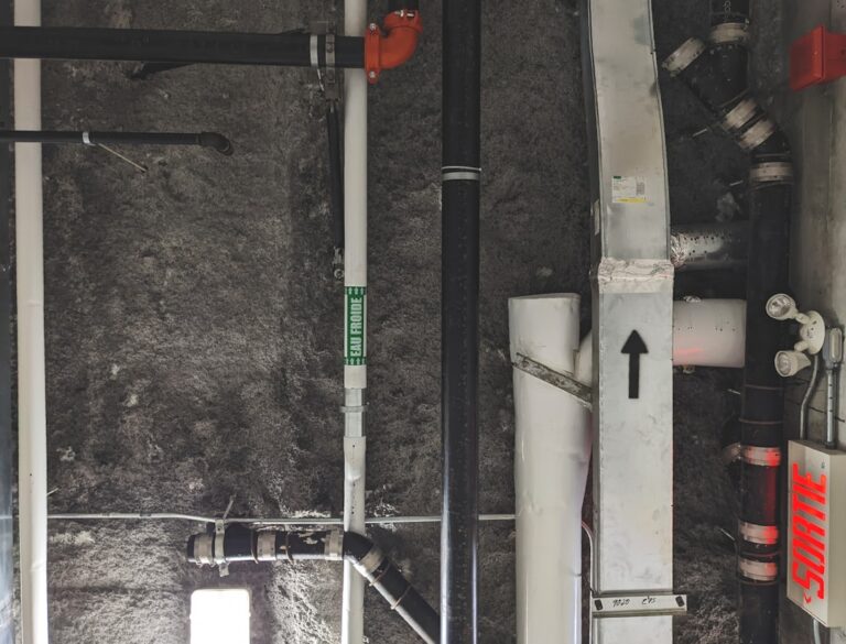 A technician installs a white PVC radon vent pipe in a residential basement utility area.