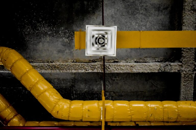 A technician installing a white pipe radon mitigation system in a residential basement with concrete walls.