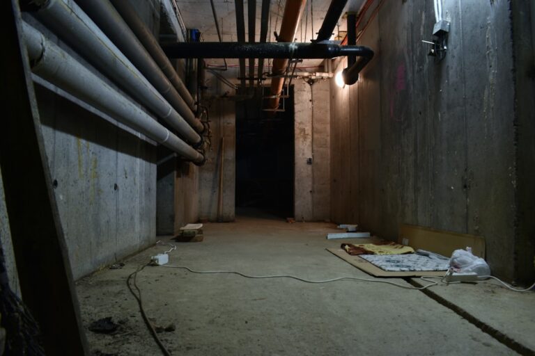 A person places a small radon test kit on a finished basement floor next to a cozy seating area.
